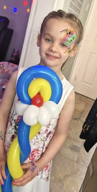 Girl holding a rainbow balloon with her face painted in Telford